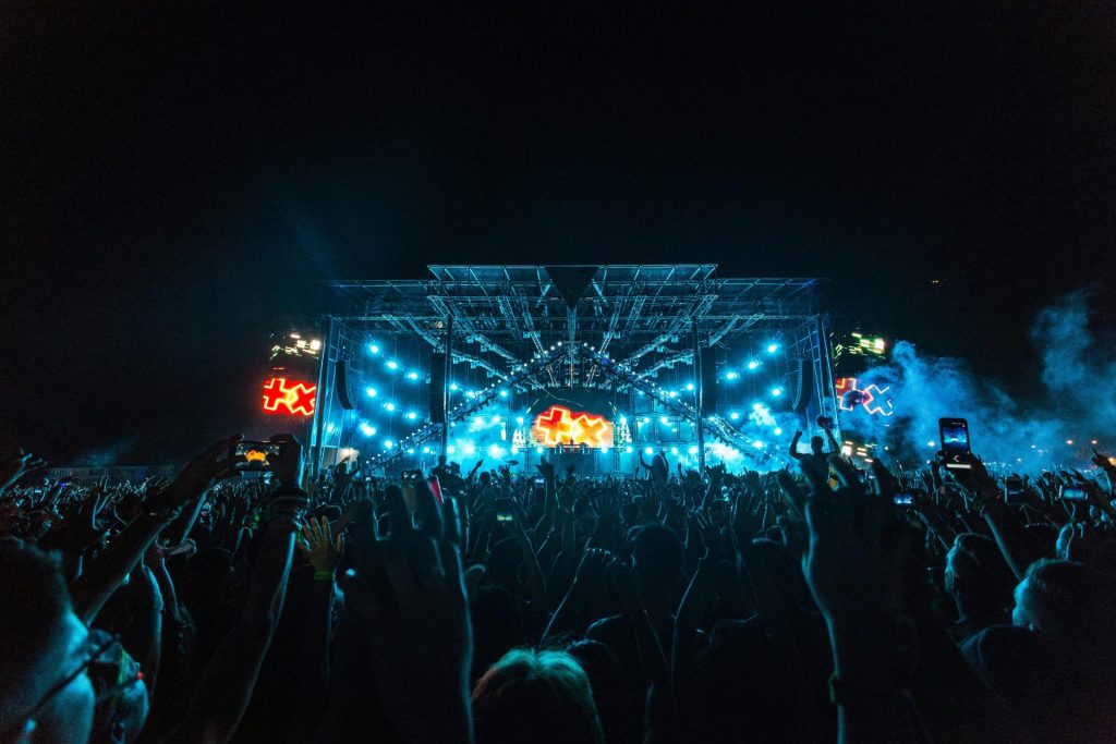 Vibrant crowd enjoying an epic concert under bright stage lights with smoke effects.